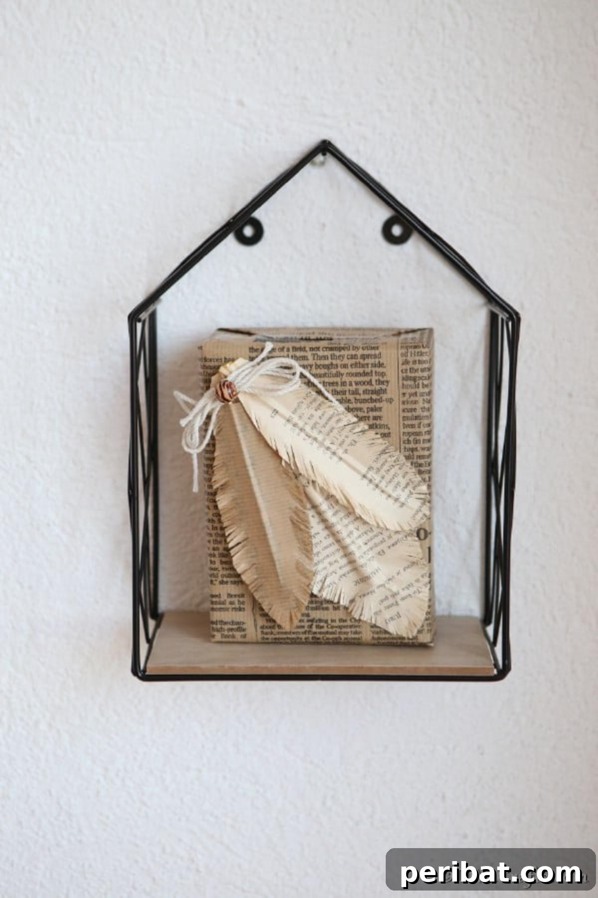 A black wire shelf on a wall, adorned with a decorative book featuring handmade paper feathers, showcasing creative home decor.