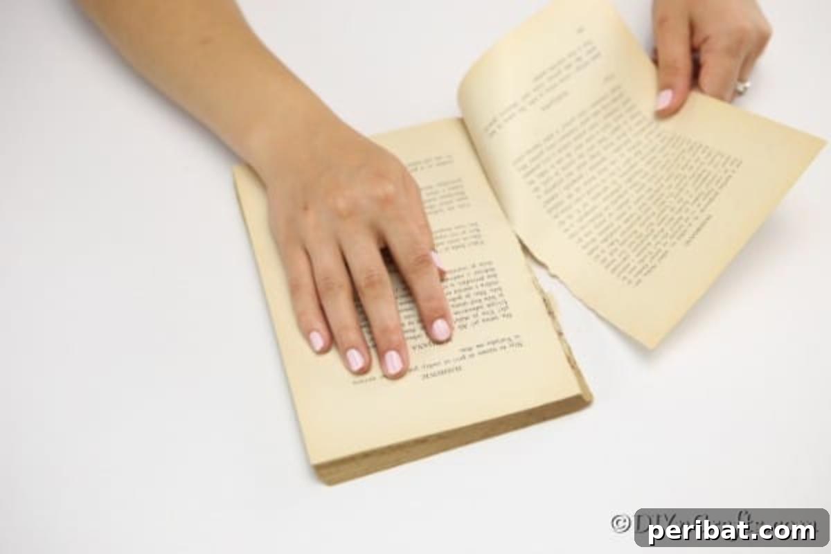 A hand gently removing pages from an old, worn book, preparing them for a craft project.