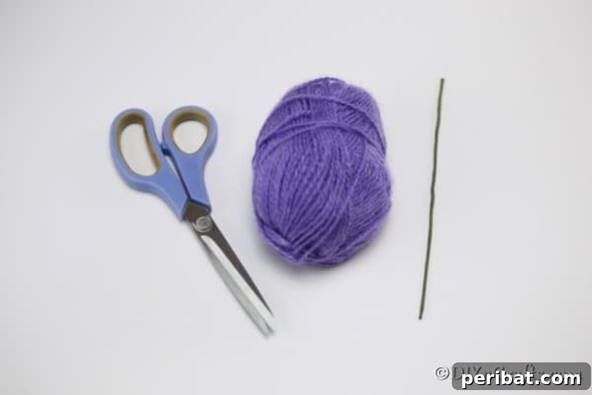 A neatly organized collection of craft supplies, including vibrant skeins of yarn, green floral wire, sharp scissors, and a hot glue gun, ready for making yarn pom pom flowers.