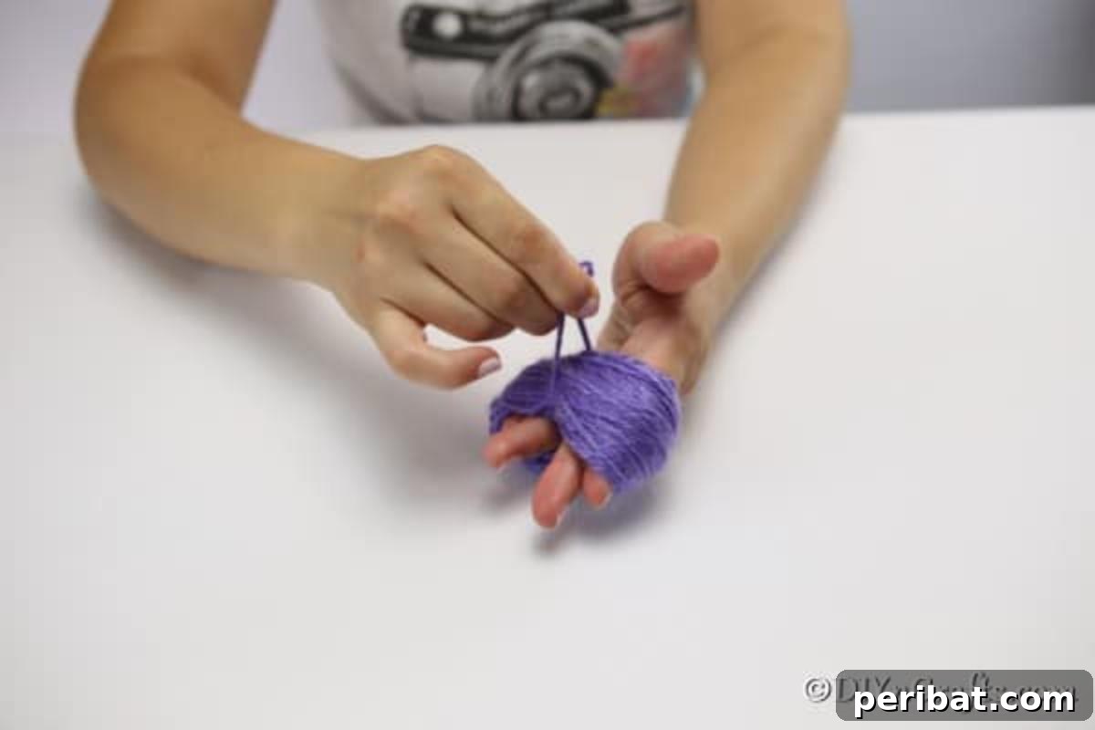 Close-up of hands carefully clipping the end of a wrapped yarn bundle, preparing to create a fluffy yarn flower.