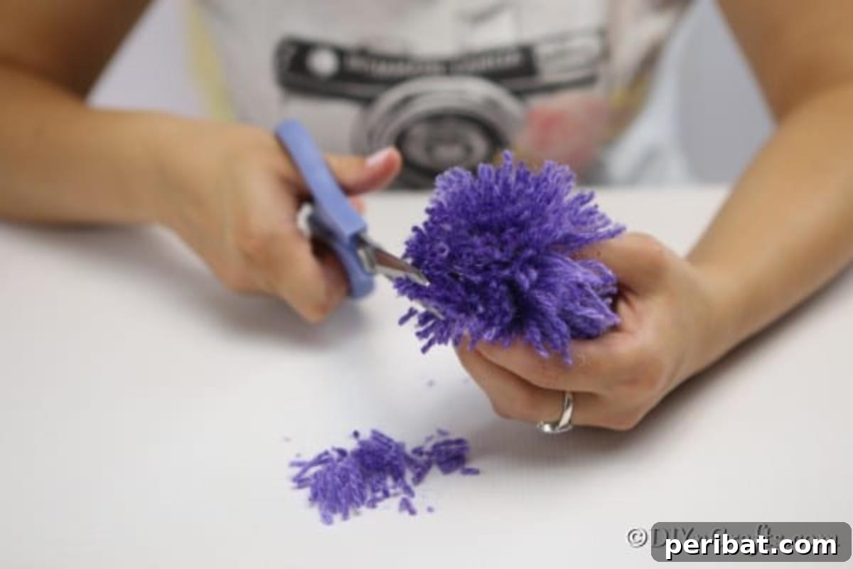 Detailed shot of scissors precisely cutting the looped ends of a yarn bundle to transform it into a fluffy pom pom flower.