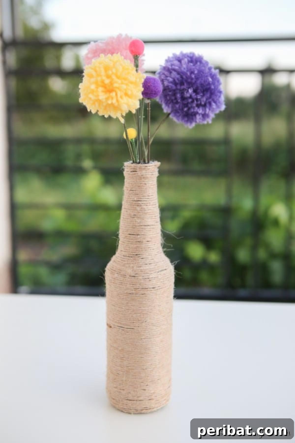 A charming rustic vase filled with a vibrant bouquet of handmade yarn pom pom flowers, creating a cozy and colorful home decor accent.
