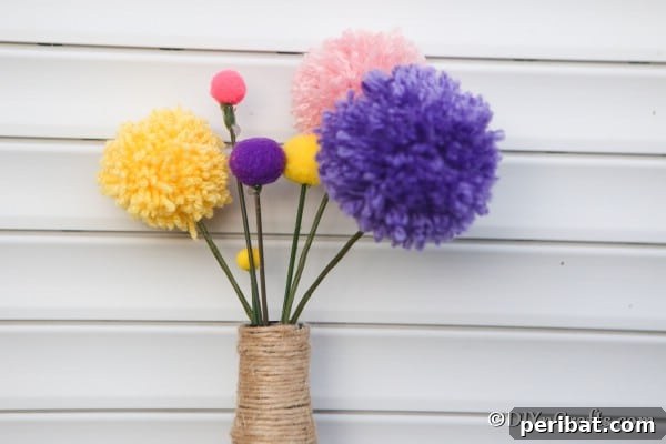A charming bouquet of colorful pom pom flowers displayed against a clean white wall, radiating warmth and handmade beauty.