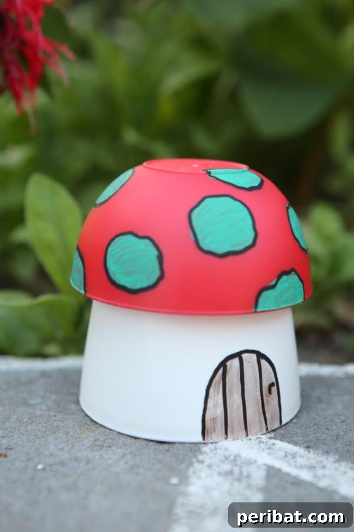 Whimsical Hand-Painted Mushroom Garden Planter 12 An up-close picture of a charming mushroom planter fairy house garden decoration placed on a sidewalk near shrubbery