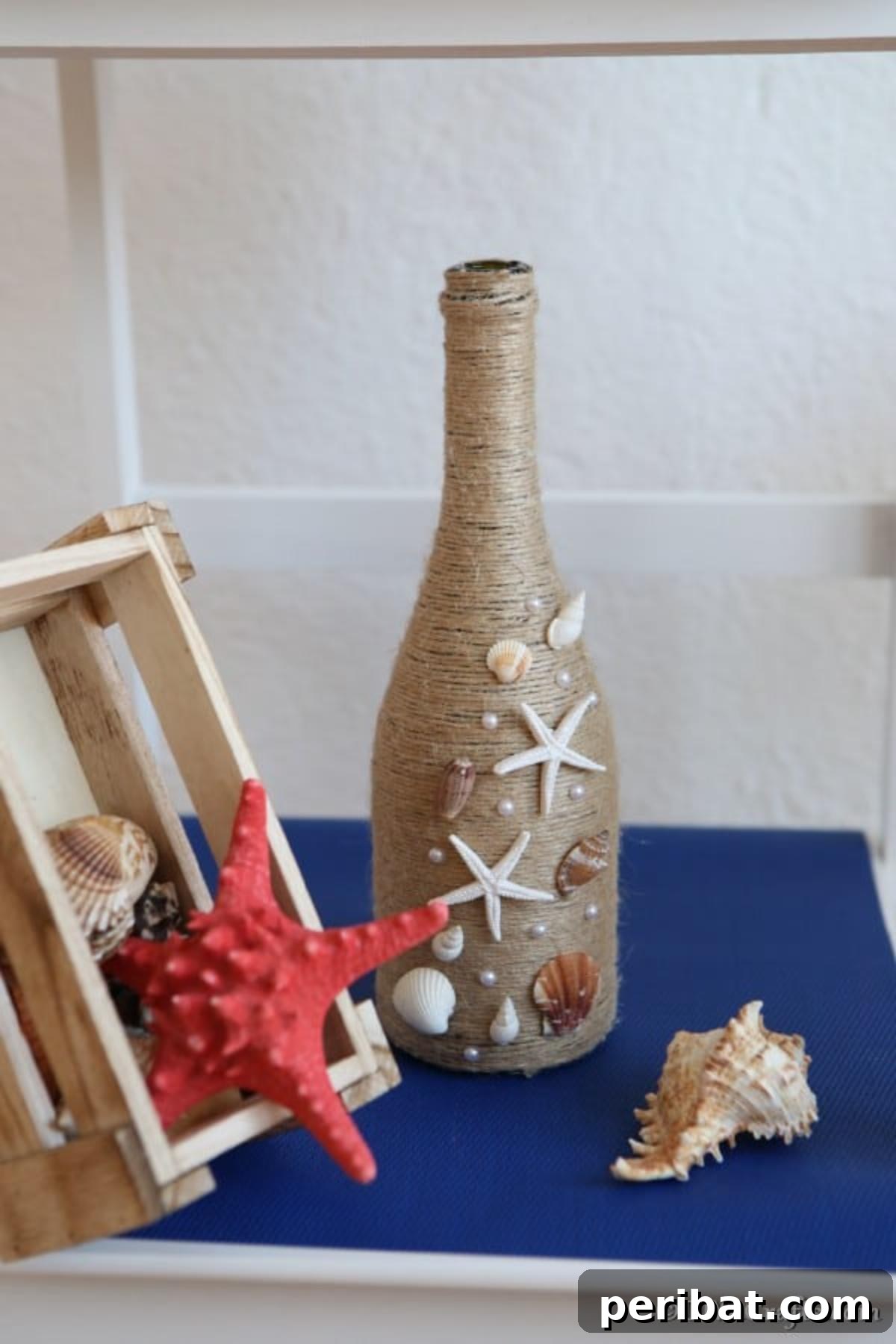 Coastal Rustic Wine Bottle Charm 6 A stunning piece of nautical wine bottle decor, featuring twine and seashells, elegantly displayed on a vibrant blue shelf alongside other coastal accents.