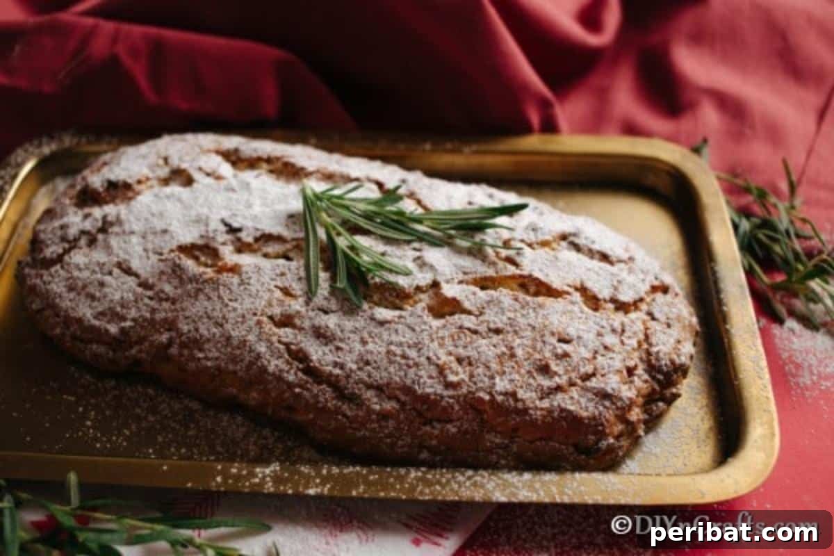 German Christmas Stollen Festive Bread Recipe 3 A freshly baked loaf of homemade Christmas Stollen on a baking sheet, dusted with powdered sugar and garnished with herbs