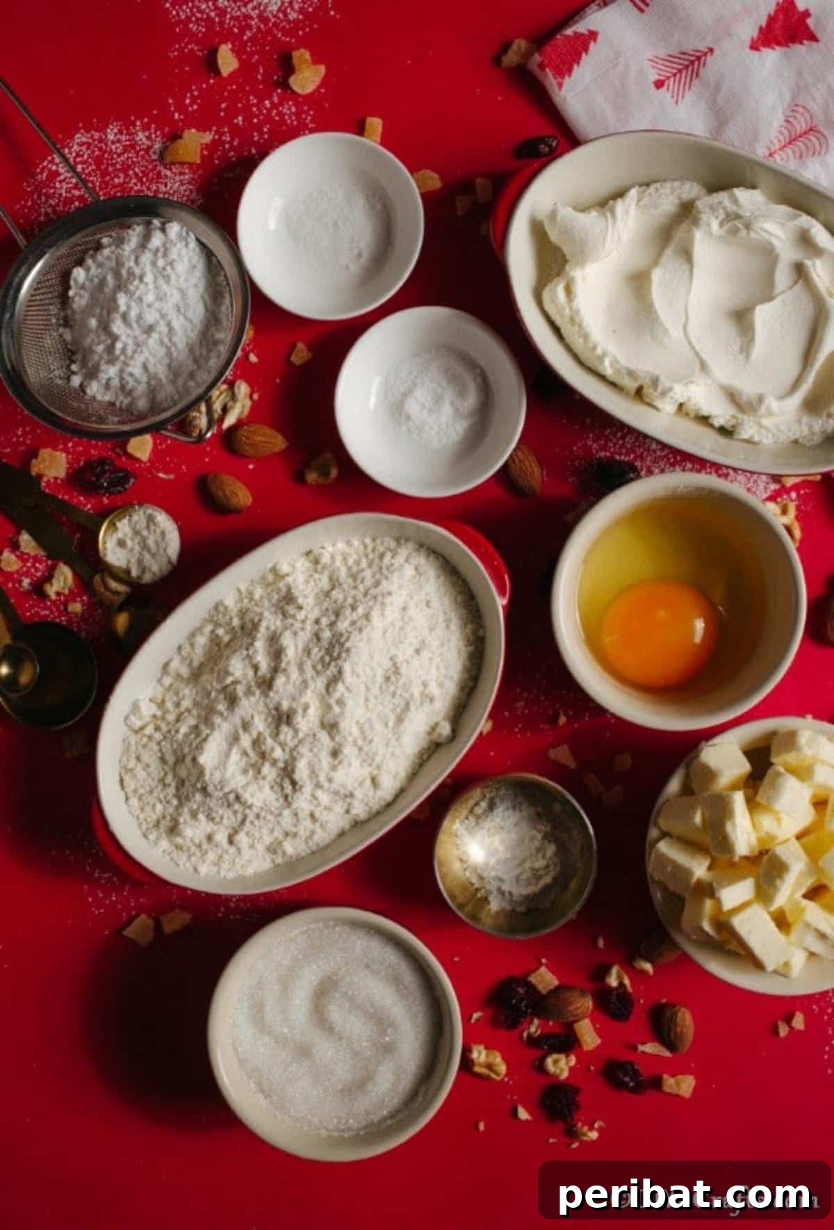 German Christmas Stollen Festive Bread Recipe 7 Various ingredients for Christmas Stollen laid out on a festive red tablecloth, including butter, sugar, flour, nuts, and dried fruit