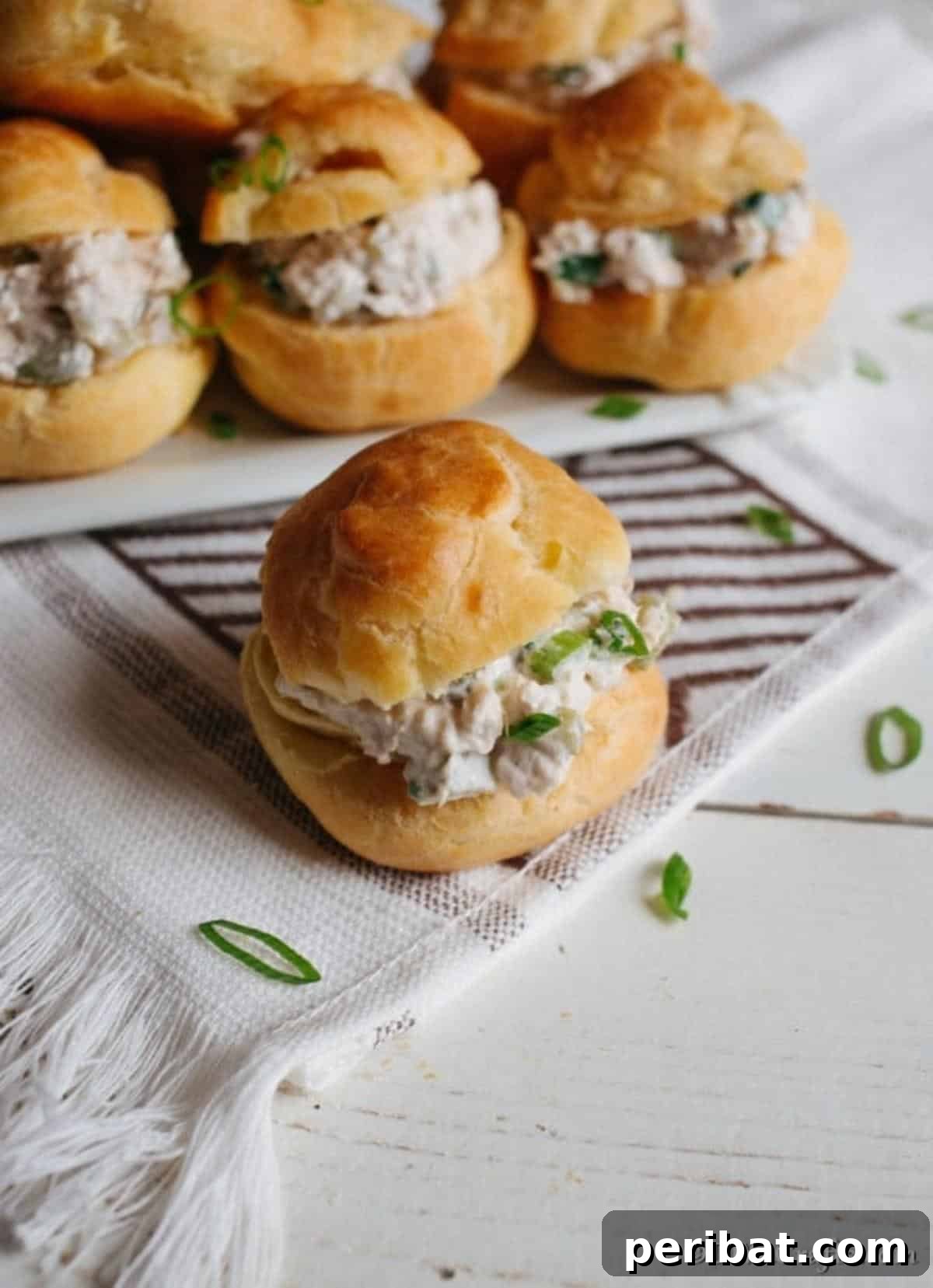 Golden Puffs, Creamy Chicken Salad 6 A single chicken salad sandwich on a black and white napkin in front of a platter of sandwiches