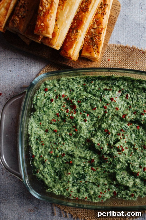 Large glass bowl filled with hot spinach dip and breadsticks for dipping