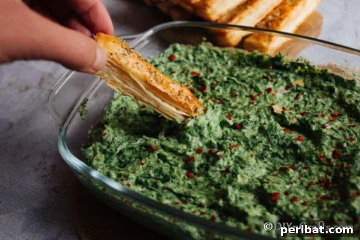 Hot spinach dip in a large clear bowl with breadstick dipping into it