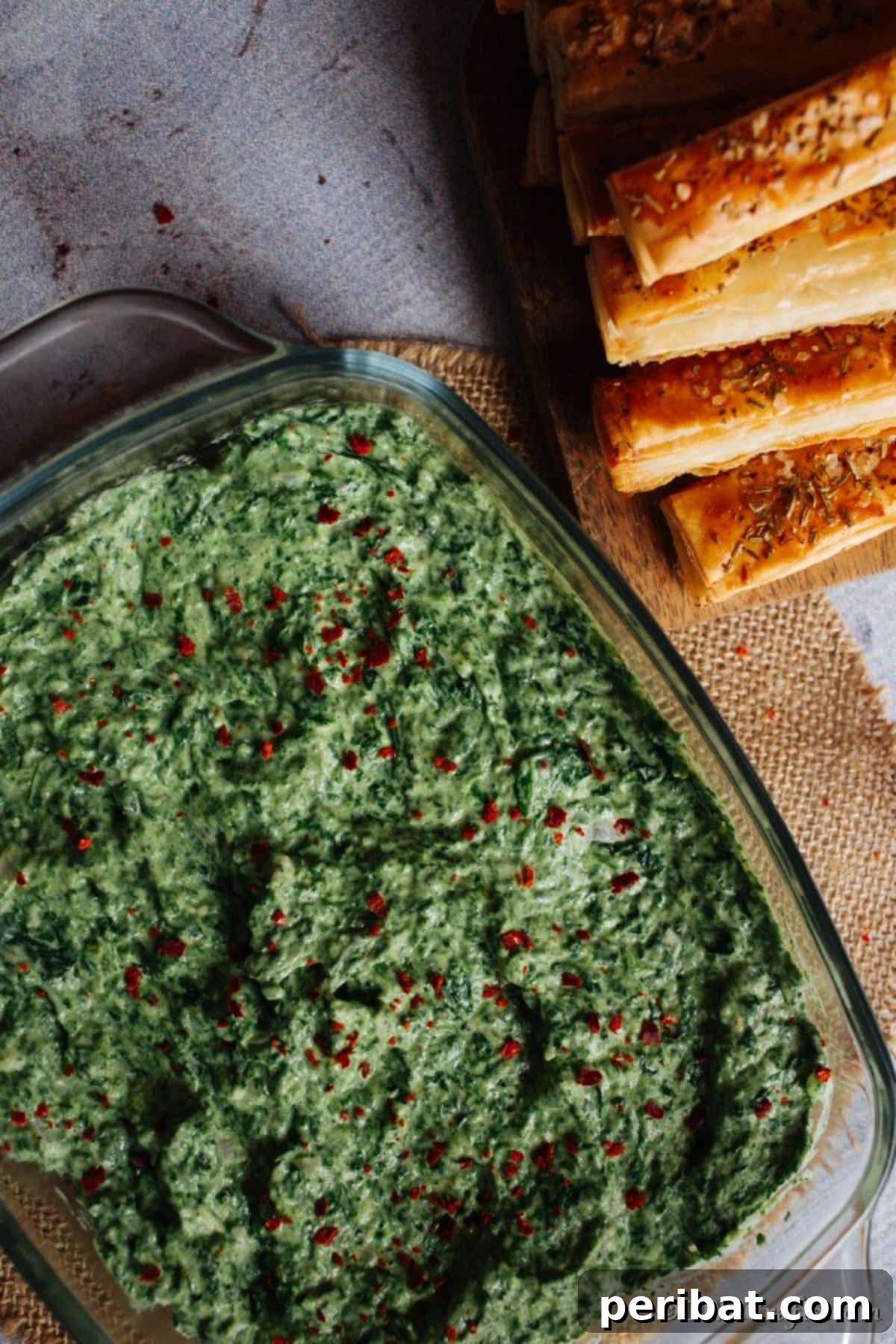 Overhead picture of a large baking dish filled with hot spinach dip with breadsticks on the side