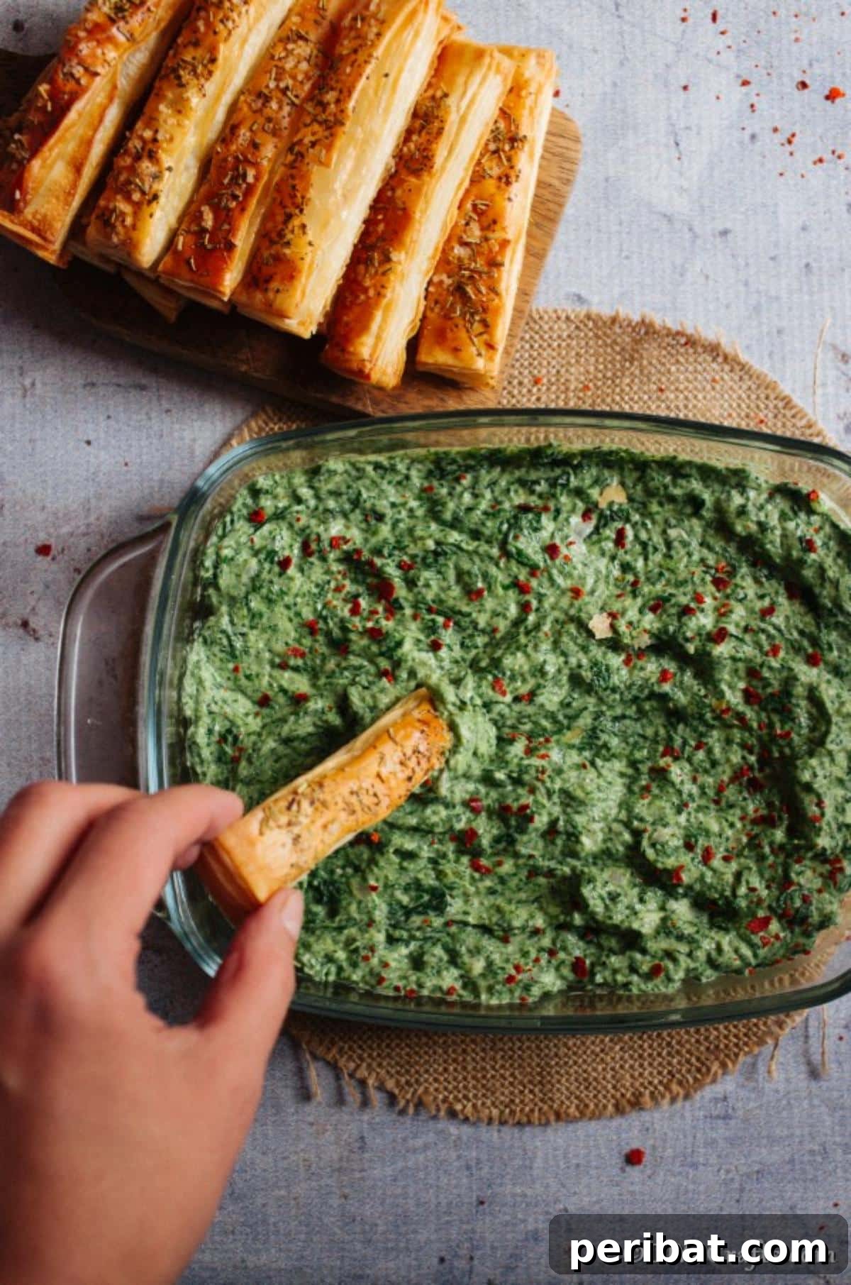 A hand holding a breadstick dipping into the hot spinach dip