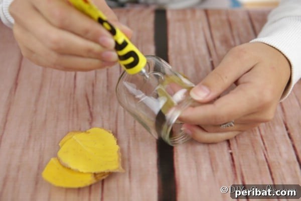 Gluing leaves onto glass jar for mason jar lantern crafts, demonstrating the adhesive application