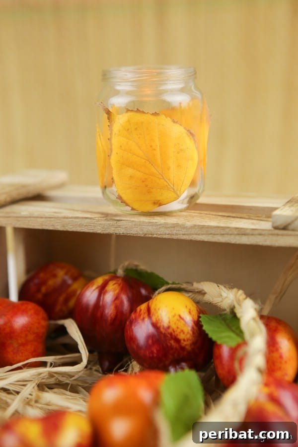 A wooden box of apples with a fall leaf candle lanterns craft sitting on top, demonstrating a decorative arrangement