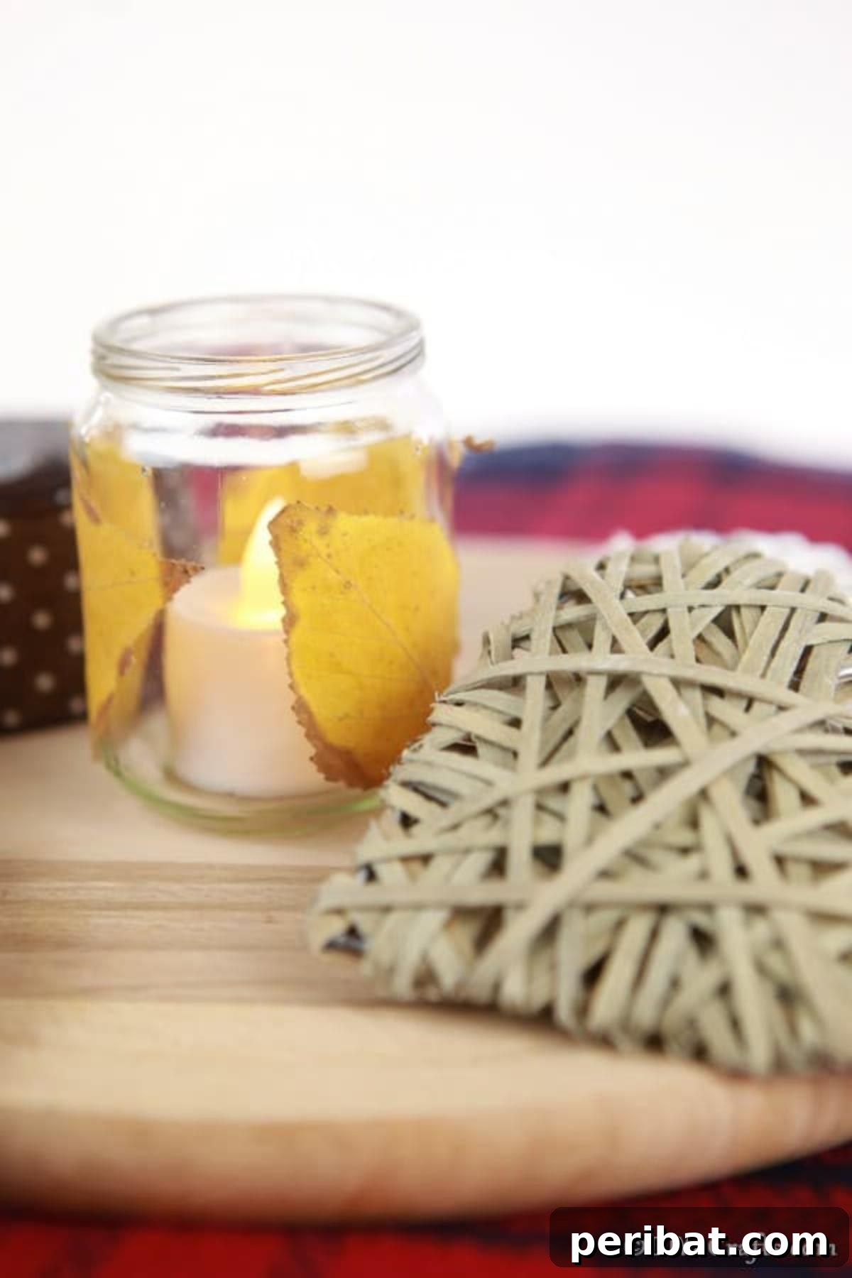 A single fall leaf candle lantern in a small jar, displayed on a wooden board against a red plaid tablecloth, enhancing its cozy appeal