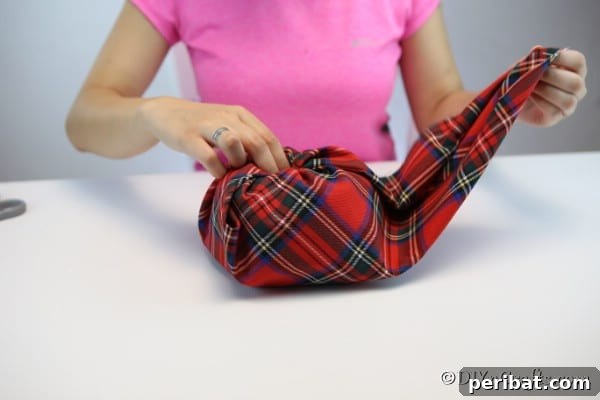 Close-up of the fabric pumpkin being wrapped, with the fabric being carefully tucked into the toilet paper roll's center.