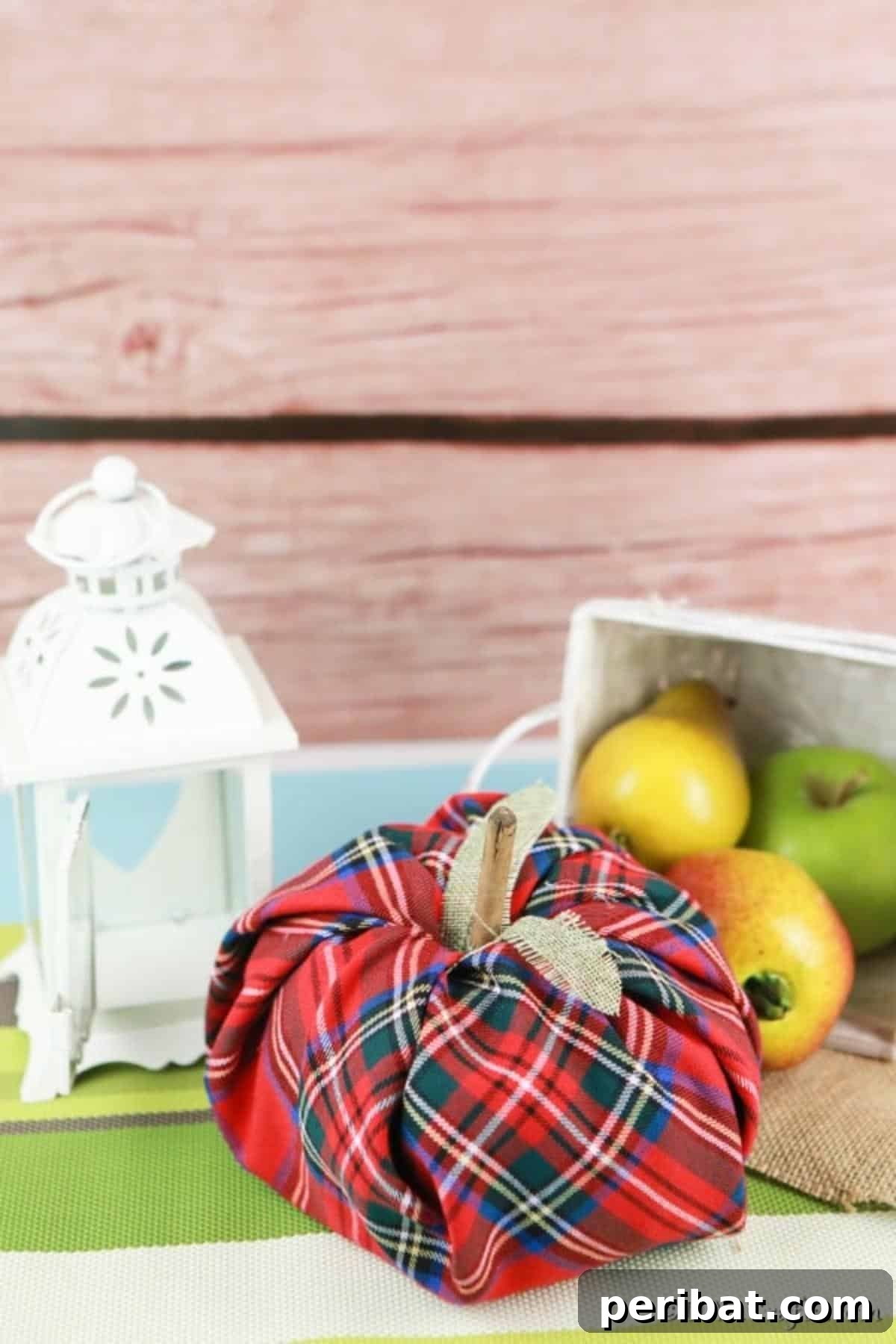 A decorative fabric pumpkin with a soft, textured fabric, displayed on a smooth green surface next to a white woven basket, highlighting its clean and appealing design.