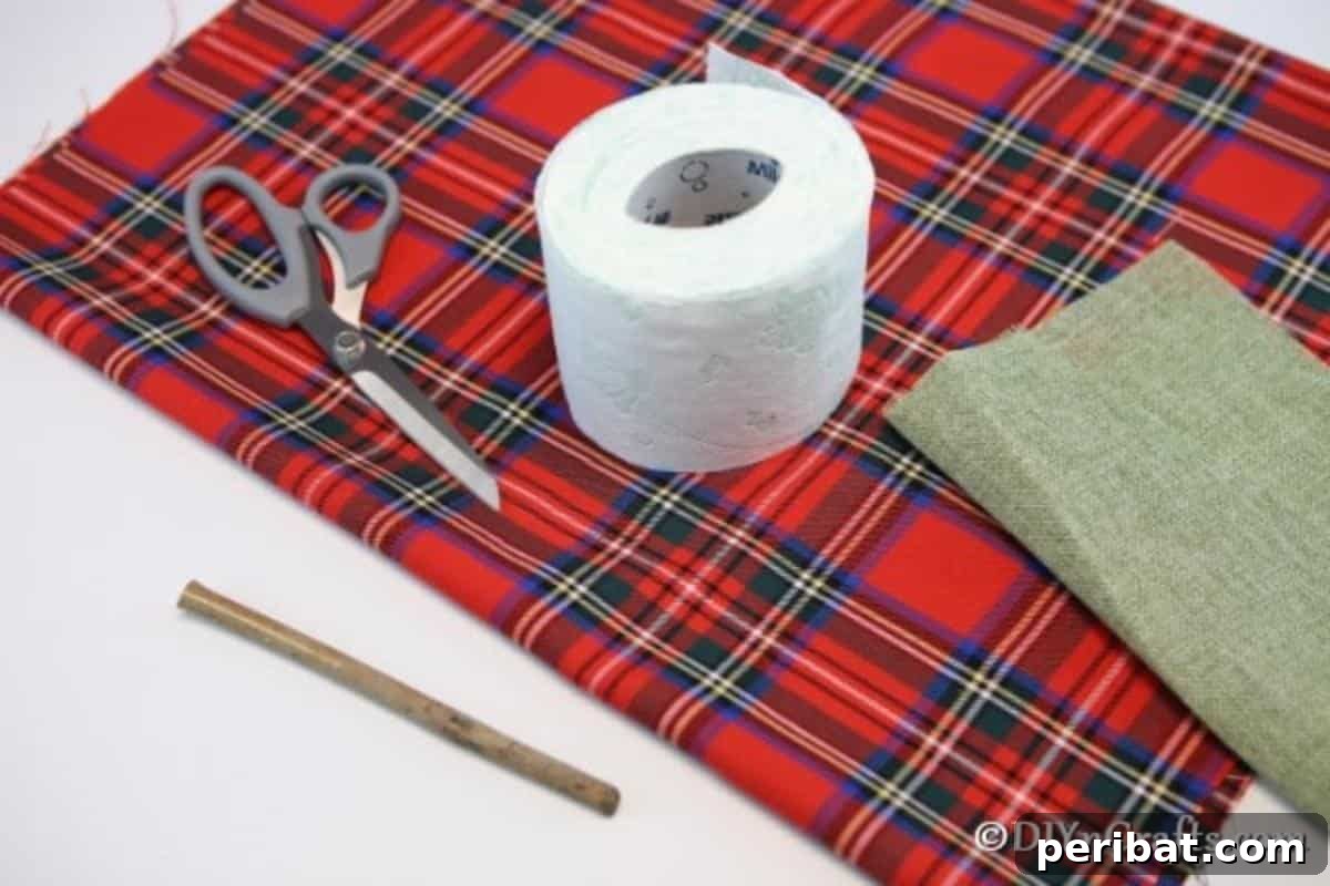 A neat arrangement of the simple supplies needed to create a fabric pumpkin: a roll of toilet paper, a square of plaid fabric, scissors, and a small twig.
