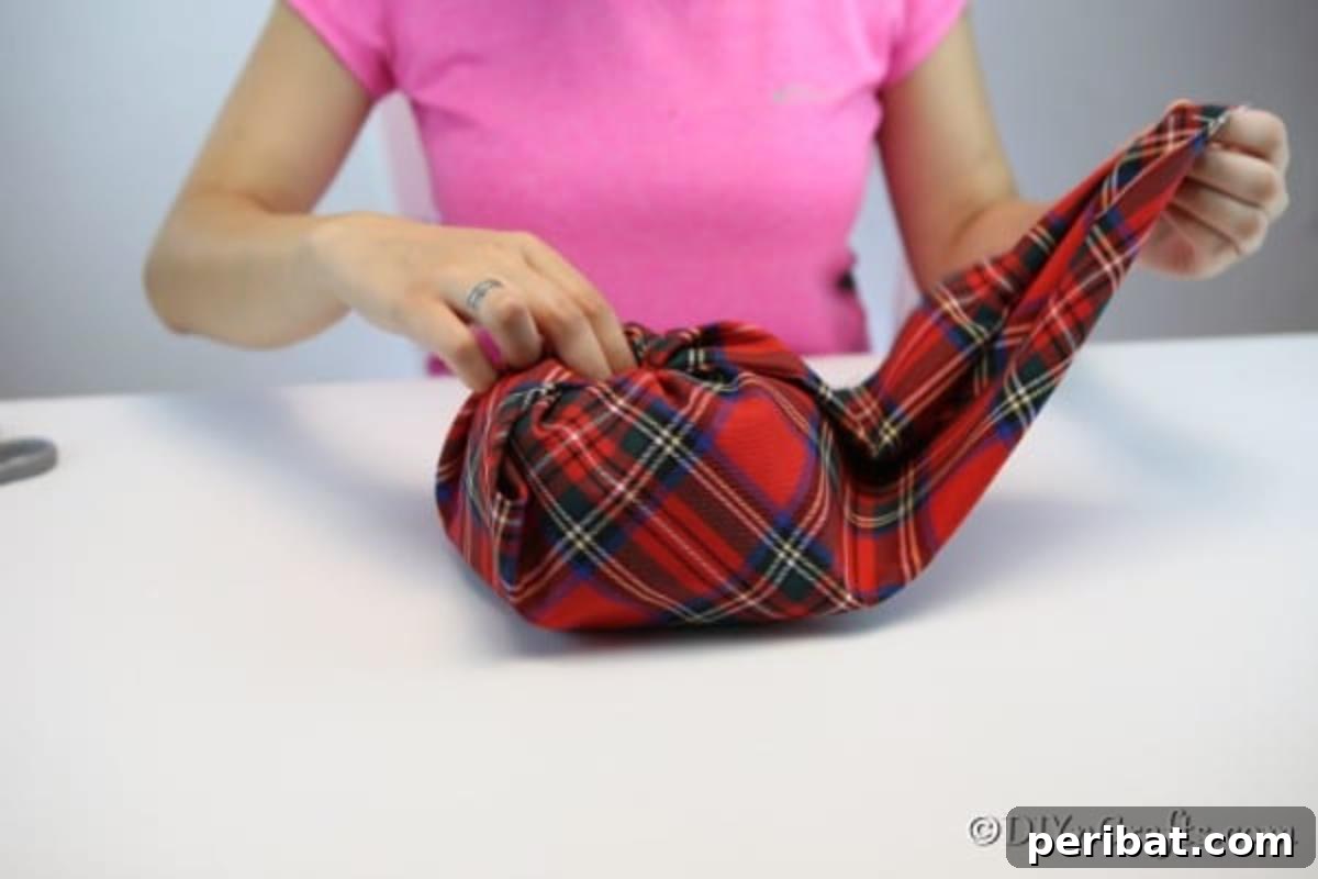 The process of wrapping the fabric around the toilet paper core to form the pumpkin, showing the fabric being tucked into the center.