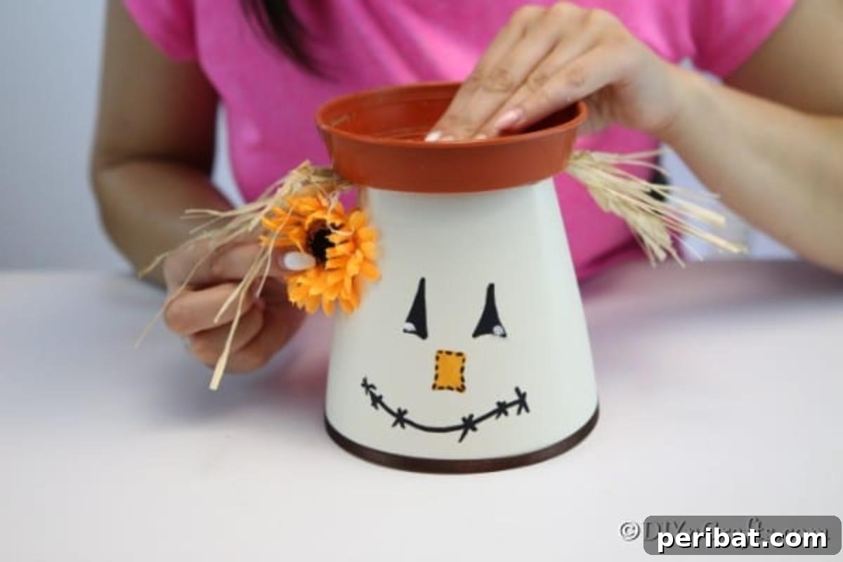 Whimsical Scarecrow Pot Lantern 10 A crafter meticulously securing the plastic planter tray, adorned with decorative hay to create the scarecrow's 'hair,' onto the top of the clay pot, forming the scarecrow's distinctive hat.