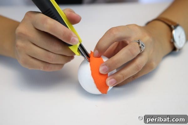 Tucking fabric edges into the grooves of the Styrofoam ball using a craft knife, securing the first segment of the pumpkin ornament