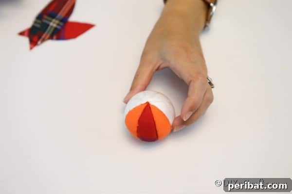 Progress shot of adding fabric to the pumpkin ornament craft, showing alternating patterns and the meticulous tucking process for a seamless finish