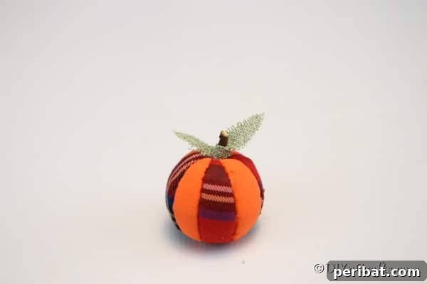 A beautifully completed fabric pumpkin ornament sitting on a clean white surface, showcasing the added twig stem and optional fabric leaf, ready for fall decor