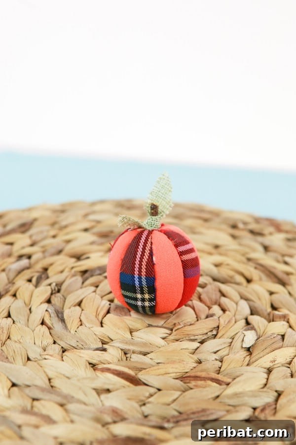 A charming fabric pumpkin ornament covered in scrap fabric, displayed elegantly on a woven mat, showcasing its handmade beauty for fall decorations