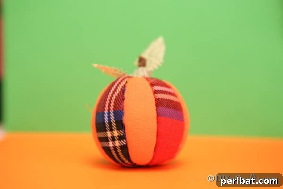 A charming DIY fabric pumpkin ornament sitting on an orange surface with a soft green background, highlighting its texture and design