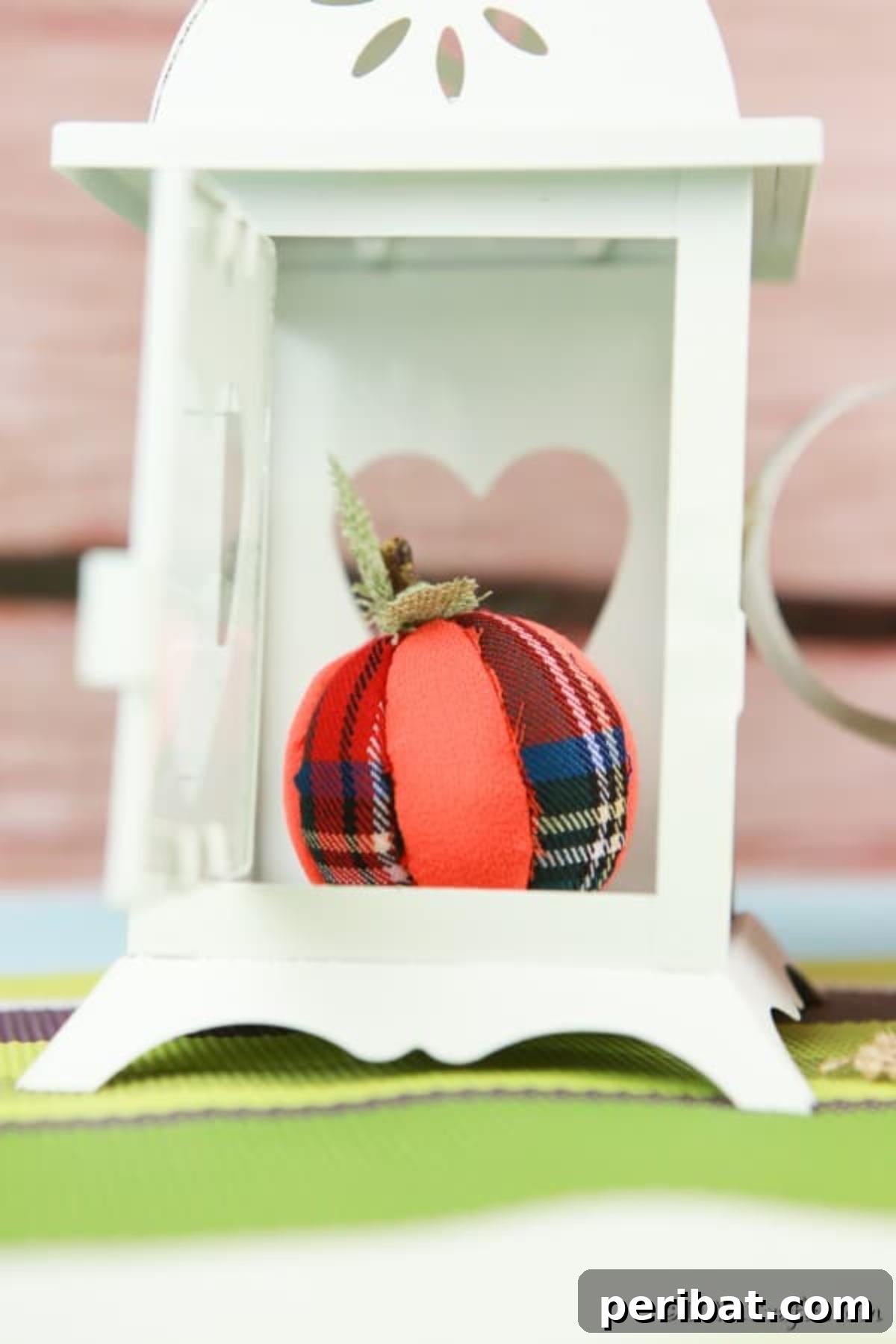 A handmade cloth pumpkin ornament creatively displayed inside a decorative white lantern holder, perfect for fall table decor