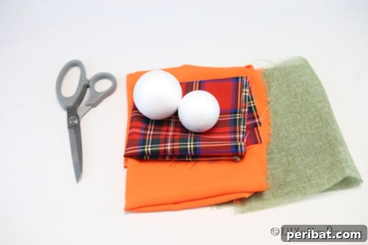 A flat lay of all the essential supplies needed for making a cloth pumpkin ornament, including a styrofoam ball, various fabric scraps, a small twig, craft knife, and scissors, arranged neatly on a crafting surface for fall decor