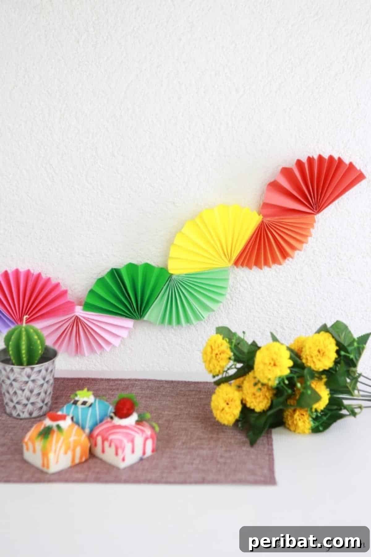 Colorful paper fan garland in rainbow hues gracefully adorning a wall behind a beautifully set dessert buffet.