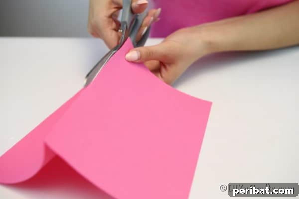 A pair of hands demonstrating the initial steps of folding and cutting paper, essential for crafting a fan garland.