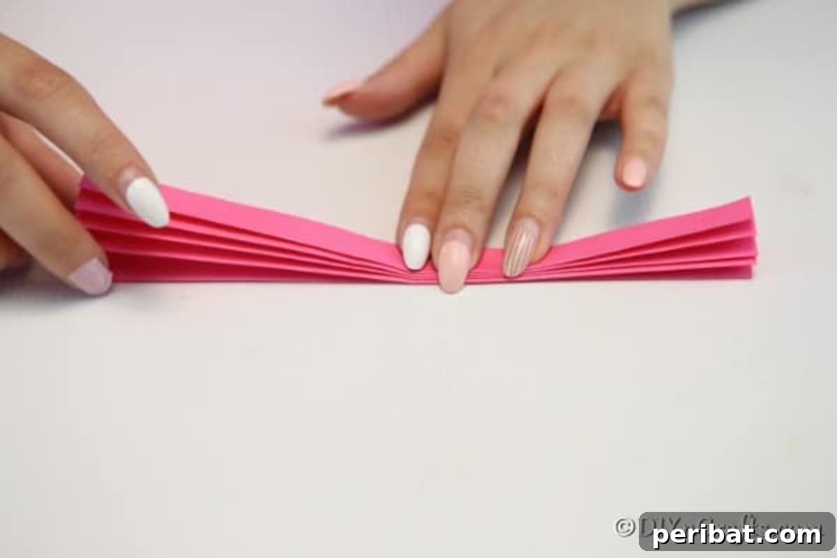 Close-up view of hands meticulously folding paper into a zig-zag pattern, demonstrating the technique to make a paper fan.