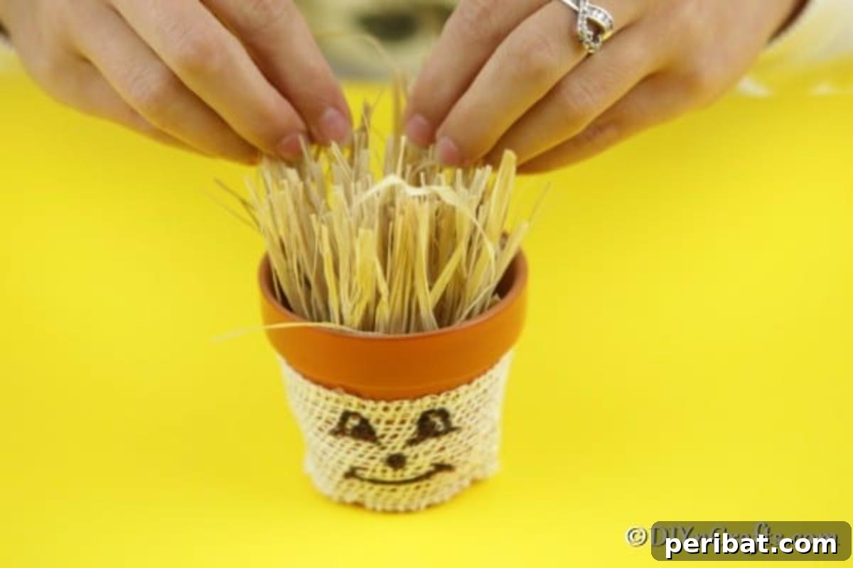 Adding decorative hay inside the scarecrow head of the flower pot person