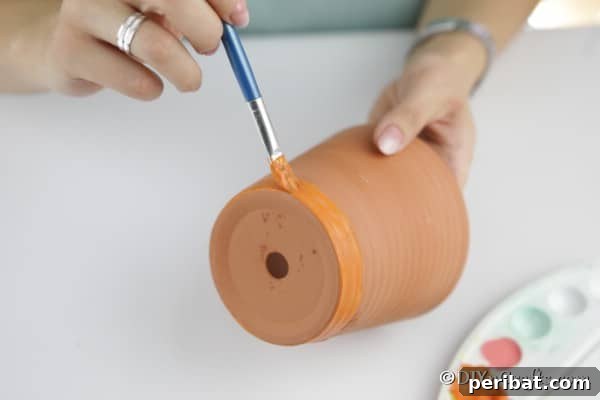 A terra cotta pot being painted vibrant orange for the pumpkin planter project