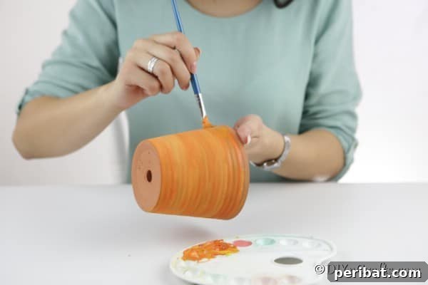 A freshly painted orange terra cotta pot drying, ready for the next steps of the pumpkin planter craft