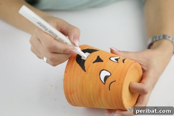 Filling in the details and colors of the silly face on the pumpkin planter project with paint pens