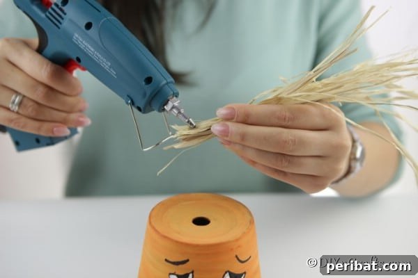 Attaching decorative hay with hot glue to the top of the clay pot pumpkin to create a stem or hair