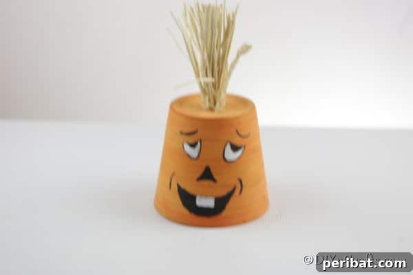 A finished silly-faced pumpkin planter, made from a terra cotta pot, displayed elegantly on a white table