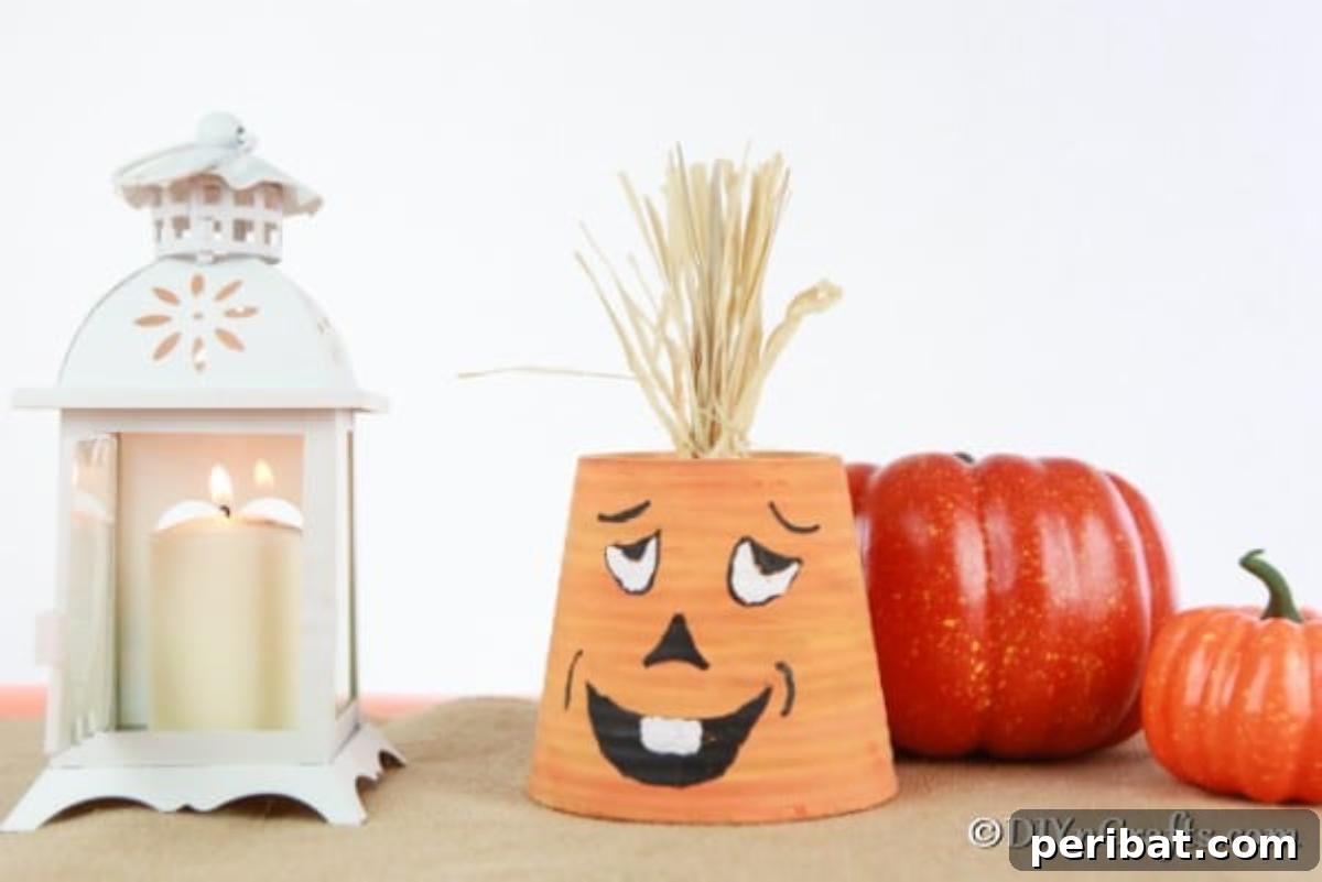 A cute, painted planter pumpkin with a silly face sitting on a table next to a smaller ceramic pumpkin and other fall decor
