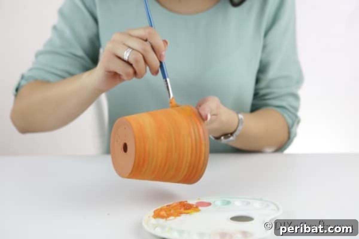 A close-up shot of a terra cotta pot being painted orange, the base color for the pumpkin planter craft