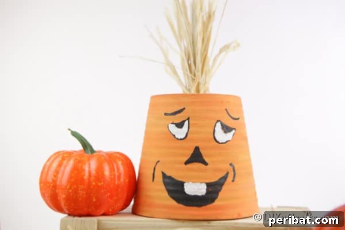 A finished silly face pumpkin planter, made from a painted terra cotta pot with decorative hay on top, resting on a wooden box with a small decorative pumpkin beside it