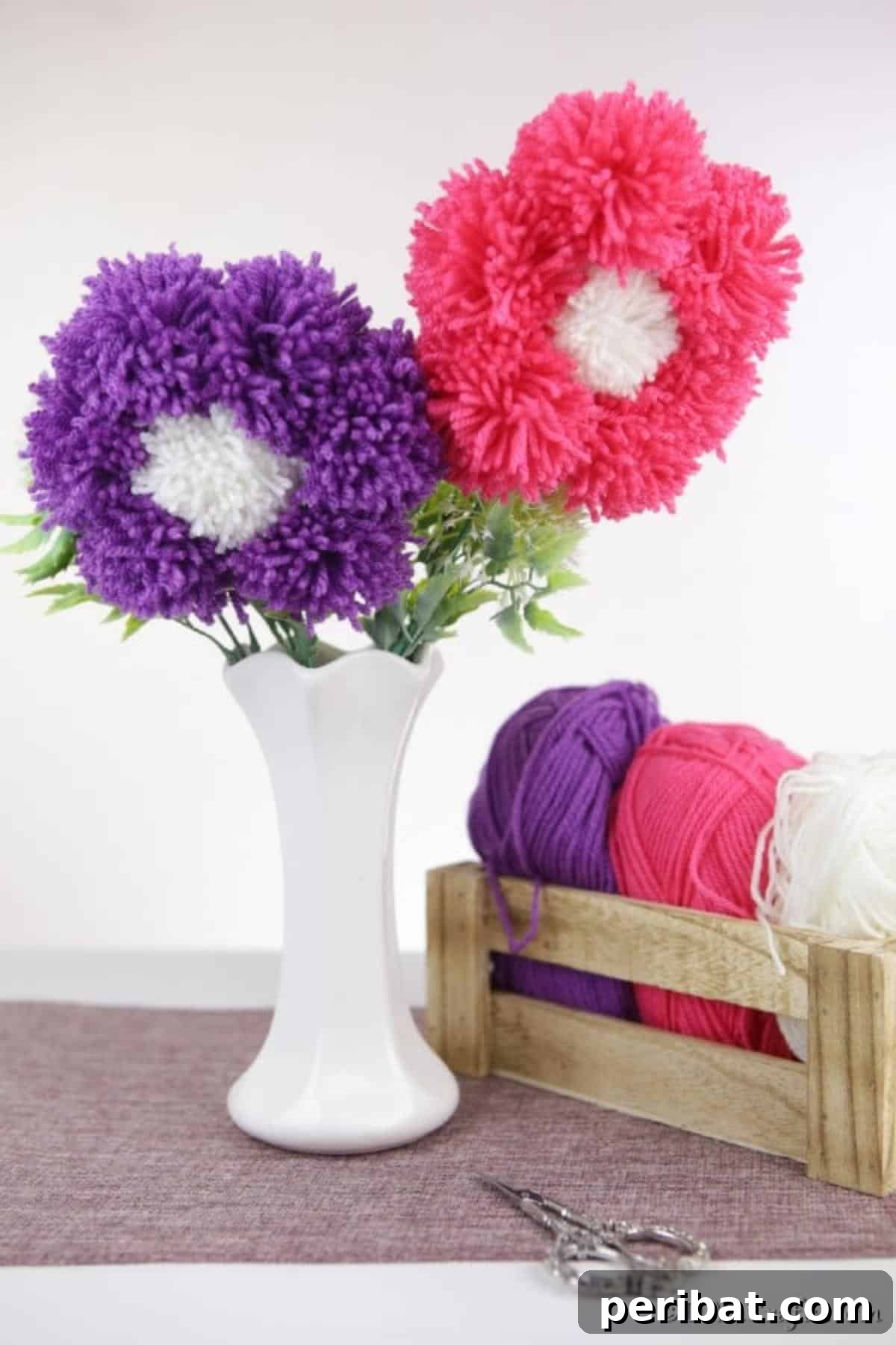 Yarn Pom-Pom Floral Displays 11 A beautifully crafted pink and purple yarn pom pom flower standing elegantly in a white vase, ready to adorn any interior.