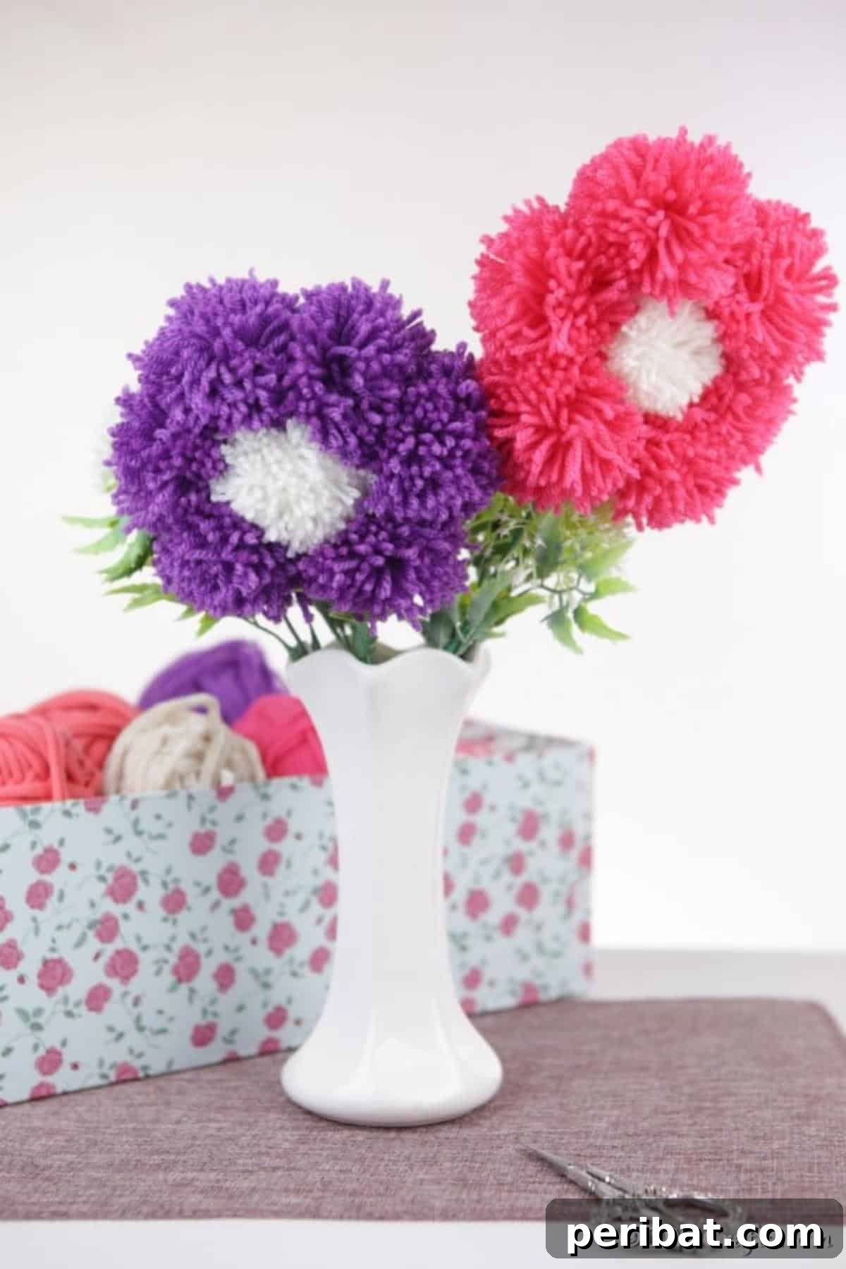 Yarn Pom-Pom Floral Displays 4 A charming white vase brimming with fluffy pink and purple yarn pom pom flowers, creating a cheerful and inviting atmosphere.
