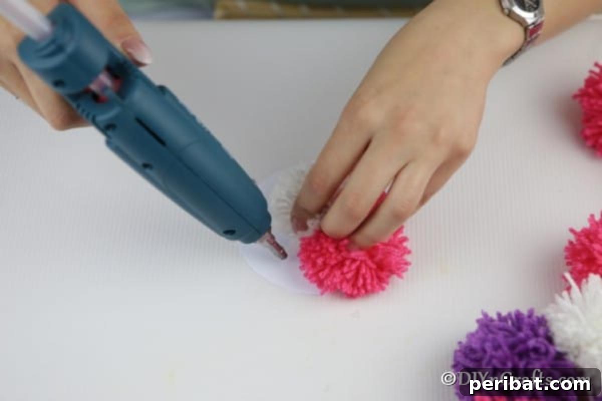 Yarn Pom-Pom Floral Displays 9 Hot glue gun securing colorful yarn pom poms onto a cardboard circle, forming the distinct shape of a handmade flower.