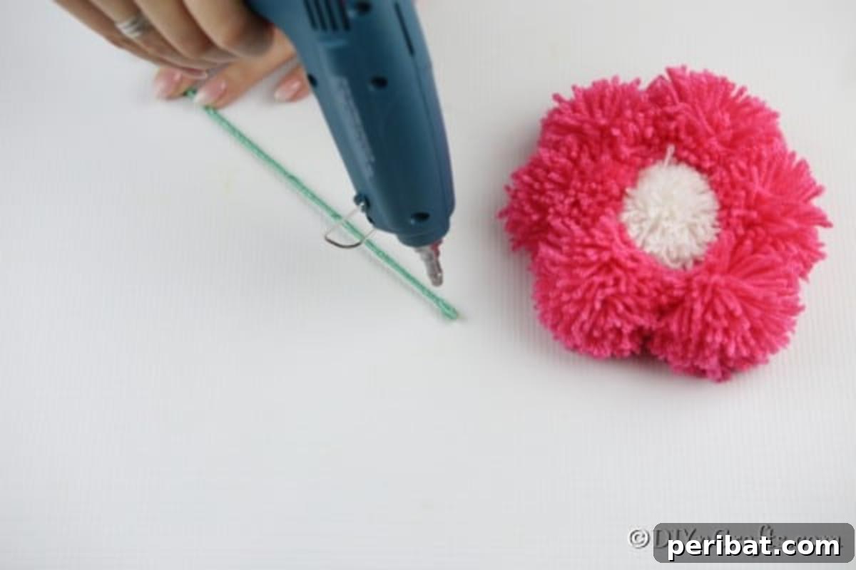 Yarn Pom-Pom Floral Displays 10 Attaching a wooden stick to the back of a yarn pom poms flower using hot glue, creating a stable stem for display.