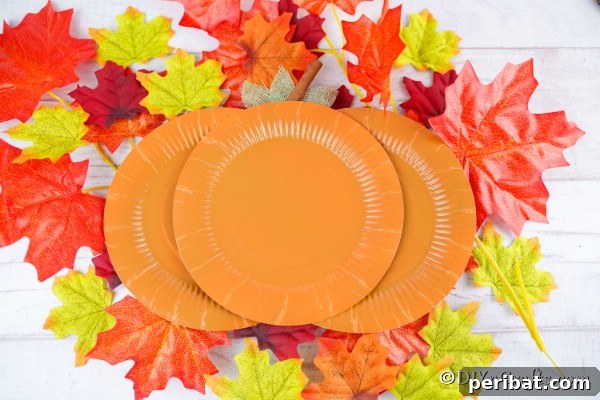 Paper plate pumpkins on a surface with leaves in the background, showcasing the finished craft.