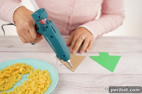 Whimsical Pasta Christmas Tree Decor 9 Gluing a piece of green construction paper to a cardboard tree shape