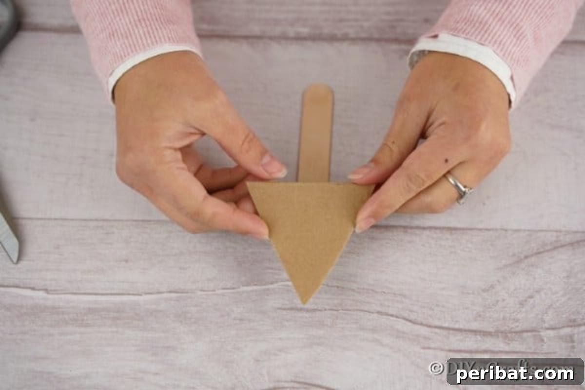 Whimsical Pom Pom Christmas Tree Decoration 7 A hand cutting a cardboard triangle to form the base for a pom pom tree ornament